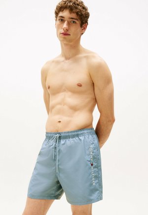 Helle blaue Badeshorts mit elastischem Bund, Kordelzug und Seitentaschen. Das "TOMMY HILFIGER"-Logo in Weiß auf der Seite bedruckt.