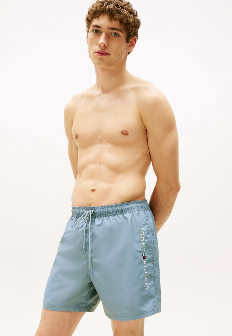 Helle blaue Badeshorts mit elastischem Bund, Kordelzug und Seitentaschen. Das "TOMMY HILFIGER"-Logo in Weiß auf der Seite bedruckt.