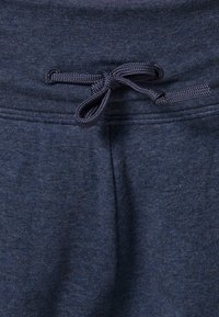 Tmavě modré bavlněné tepláky s texturovanou tkaninou, elastickým pasem se šňůrkou a viditelným šitím po stranách.