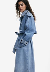 Hellblauer Jeans-Trenchcoat mit tailliertem Gürtel, großem Kragen und knöpfbaren Manschetten. Verfügt über eine glatte Textur und eine lockere Silhouette.