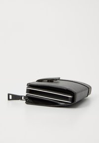 Portofel negru cu un design elegant, parțial deschis pentru a dezvălui câteva carduri metalice în interior. Așezat pe un fundal alb simplu.