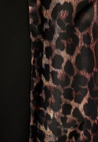 La tela de estampado de leopardo presenta una mezcla de manchas marrón oscuro y beige sobre un fondo negro, con una textura suave y un borde doblado.