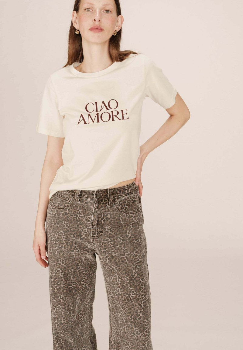 T-shirt beige avec "CIAO AMORE" imprimé en marron, associé à un jean large en imprimé léopard texturé dans des tons terreux.