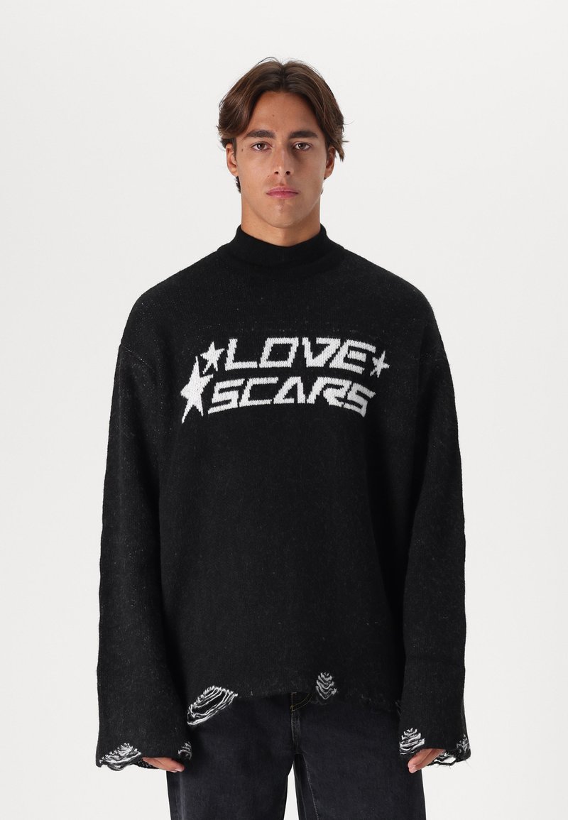 Μαύρος πλεκτός σκούφος με ψηλό γιακά, που διαθέτει λευκό κείμενο "LOVE SCARS" και γραφικά με αστέρια. Με φθαρμένες άκρες και χαλαρή εφαρμογή, υφασμάτινη υφή.
