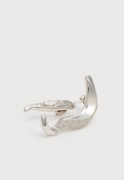 Boucles d’oreilles courbées en argent, l’une avec une rangée de petits cristaux, l’autre avec une plus grosse pierre centrale claire entourée de petits cristaux.