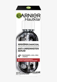 Garnier AHA BHA kolserumförpackning, genomskinlig flaska med pipett, svart serum inuti, vita accenter och grön märkning.