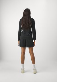 Camiseta negra de manga larga con detalles blancos, combinada con pantalones cortos de malla negros. El modelo lleva calcetines blancos y zapatos claros. El cabello es largo y ondulado.