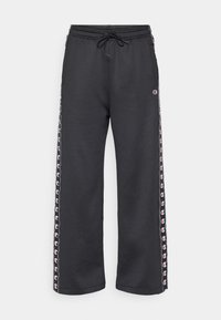 Calças de fato pretas com um corte relaxado, apresentando uma cintura com cordão e riscas laterais com detalhes em logo em vermelho e branco. Tecido de textura suave.