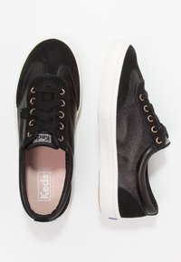 Černé tenisky s nubukem a hladkou kůží, s kovovými zlatými oky, bílou gumovou podrážkou a růžovými stélkami s logem "Keds".