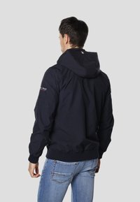Granatowa kurtka z kapturem, zapinana na zamek z przodu, z elastycznymi mankietami i talią. Posiada logo na rękawie oraz gładką, lekką tkaninę.
