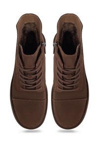 Bottes en daim marron à lacets, avec fermetures éclair latérales et doublure en fourrure, vues de dessus sur fond blanc.