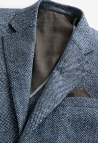 Tweed blezer s teksturom u plavoj boji sa smešanim uzorkom unutašnjosti u smešnoj boji i smešnom maramom umetnutom u džep na grudima.