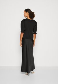 Black puff-sleeve top with a round neckline paired with a long black satin skirt; model wears patterned heels. Smooth texture, fitted design.