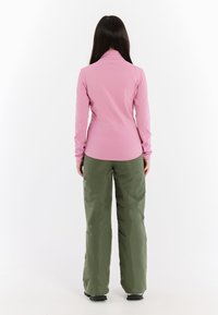 Ružový top s dlhým rukávom a golierom, spojený s voľnými zelenými nohavicami. Tkanina vyzerá hladko, vhodná na vonkajšie aktivity.
