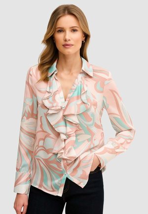 Blusa ligera de color pastel con un frente con volantes, intrincados patrones florales en rosa y verde azulado, puños abotonados y cuello con solapa.