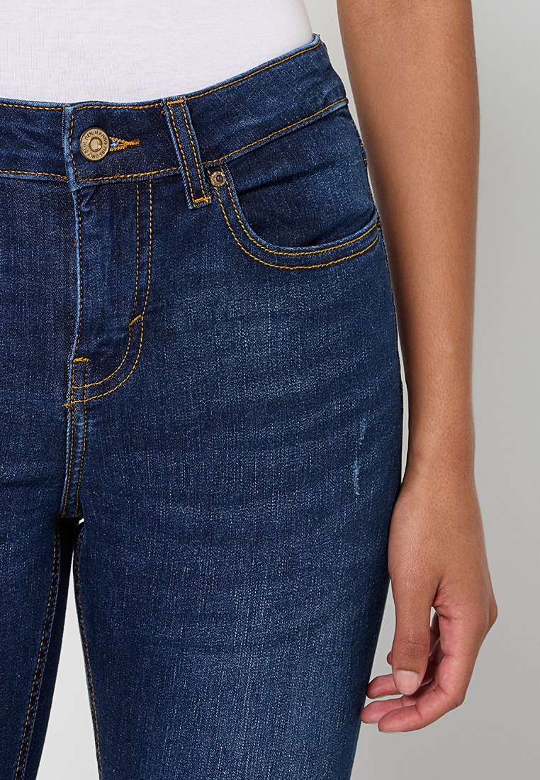 Dunkelblaue Jeans aus Denim mit strukturierten Taschen, gelben Nähten und einem Metallknopfverschluss. Glatte Textur und figurnahe Passform.