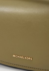 Borsa in pelle verde oliva con una finitura liscia, caratterizzata da un logo dorato "Michael Kors" e dettagli cuciti lungo il bordo.