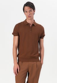 Brown knitted polo shirt with short sleeves, featuring a quarter-zip collar and ribbed hem. Paired with tailored brown trousers.