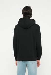 Black hoodie with a kangaroo pocket, ribbed cuffs, and hem. Made of soft fabric, featuring a simple design and a lined hood.