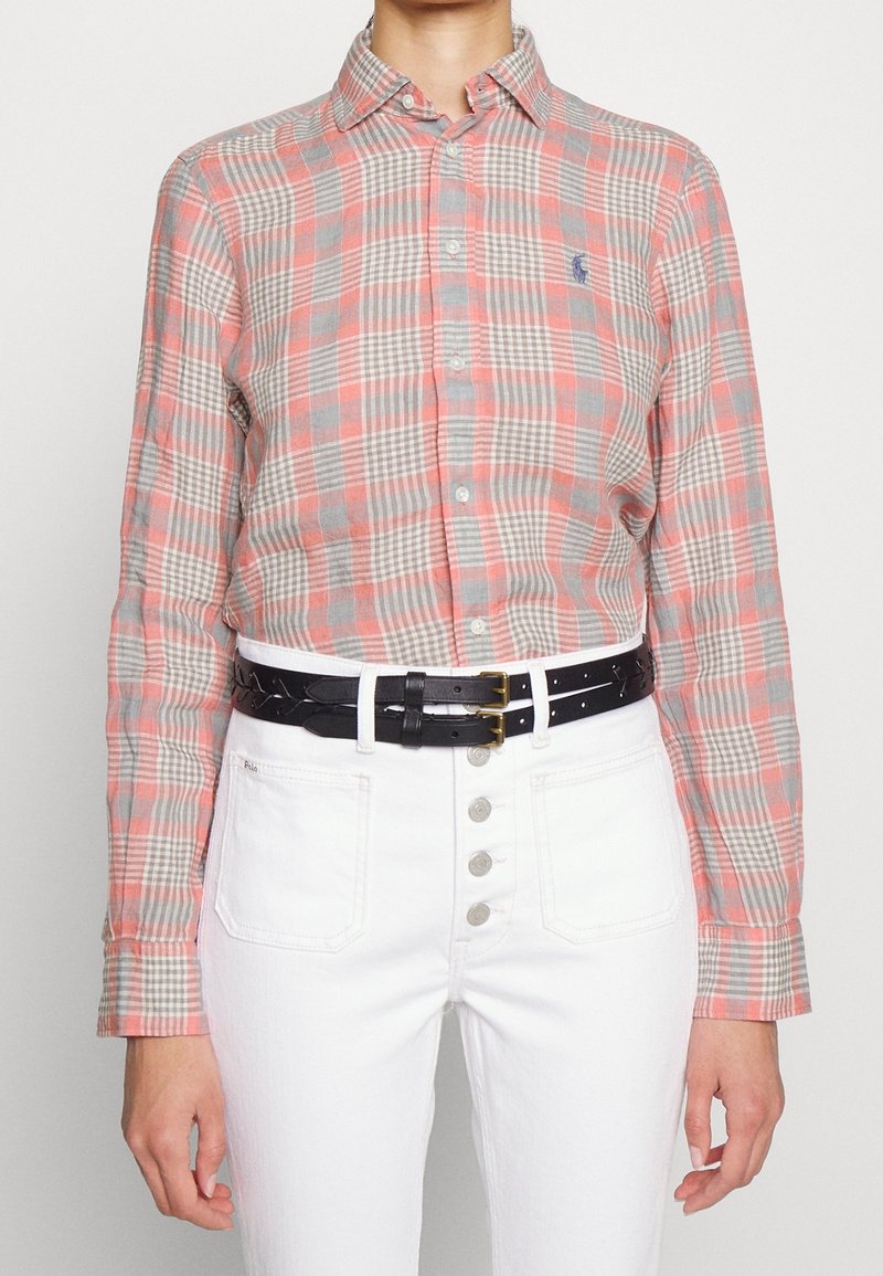 Rutig knyt skjorta i röda och grå nyanser, med klassisk krage och långa ärmar. Bärs med ett svart flätat bälte och vita högmidjade jeans.