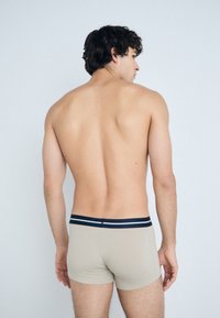 Beige boxer alsónadrág, sötétkék csíkos derékkal, testhezálló fazonban és sima textúrával, hátulról látható egy modellen, világos háttérrel.