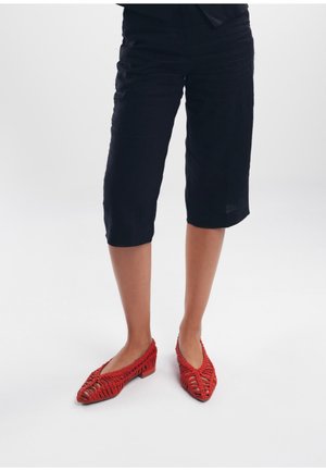 Czerwone, plecione baleriny z otwartym zdobieniem i niewielkim obcasem, w połączeniu z czarnymi, skróconymi spodniami z lekkiego materiału.