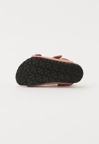 Rosa mockaskinnsandaler med svarta gummisulor som har ett vågigt mönster. Remmar med en platt design och utan synlig hårdvara eller dekorationer.