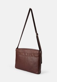 Brązowa skórzana torba listonoszka o płaskim kształcie, regulowanym pasku na ramię i przednich kieszeniach. Gładka tekstura z minimalnymi detalami przeszyć.