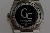 Montre-bracelet en acier inoxydable avec un cadran circulaire noir, des accents argentés et des détails gravés incluant le logo "Gc" et une résistance à l'eau de 100 mètres.