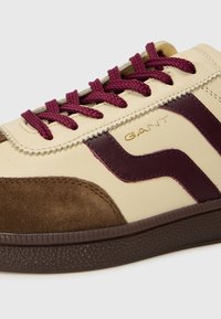 Tenis sportivi cu partea superioară din piele crem, accente bordo, vârf din suede maro și șireturi burgundy. Talpă din cauciuc texturat maro.