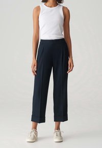 Un haut sans manches blanc associé à un pantalon large bleu marine avec un ourlet retroussé, porté avec des baskets beiges. Texture lisse et design décontracté.