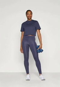 Marineblå kort t-skjorte og høytlivs leggins, begge i glatt stoff. Modellen holder lyseblå manualer og har på seg hvite trening-sko.