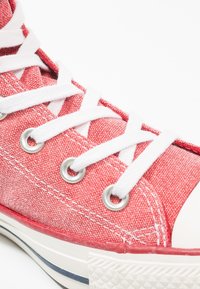 Czerwone płócienne sneakersy za kostkę z białymi sznurówkami, metalowymi oczkami, teksturowaną powierzchnią, kontrastującą gumową podeszwą oraz białym noskiem.