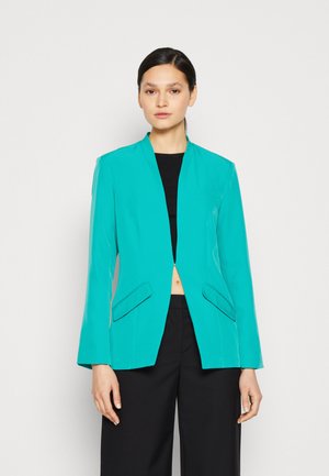 Blazer turquesa con una forma estructurada, frente abierto, mangas largas y dos bolsillos frontales. Textura suave, diseño minimalista, sin cierres.