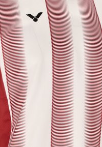 Rød og hvid atletisk t-shirt med lodrette striber og et sort logo på fronten. Fremstillet af strækbart, åndbart stof.
