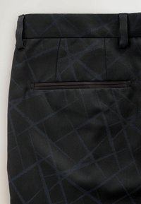 Black fabric pants featuring a geometric pattern in dark blue, with a sleek back pocket trimmed in black. Textured material, tailored finish.