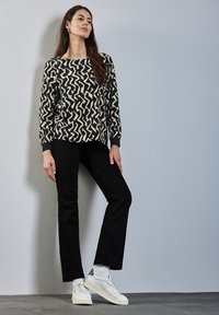 Camiseta negra de manga larga con un patrón en zigzag blanco, combinada con pantalones negros y zapatillas blancas. La tela parece suave y tiene un ligero brillo.