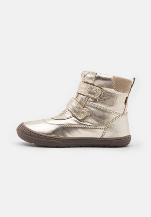 Chaussure montante en or métallique avec deux bandes Velcro et semelle en caoutchouc marron, conçue pour les enfants, vue de profil sur fond blanc.