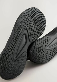 Semelles de chaussures de sport noires avec un motif de semelle texturé comportant des designs courbés et ondulés, fabriquées en matériau en caoutchouc durable.