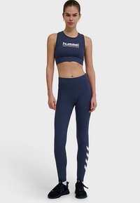 Marinblå sportset med en kort topp med logotyp och matchande leggings med en vit diagonalinje, tillverkade av ett stretchigt, slätt material.
