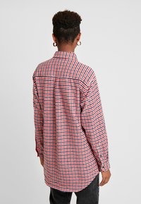 Camicia a scacchi rossa e blu con colletto, polsini con bottoni e orlo curvo. Realizzata in tessuto con una trama a rilievo.