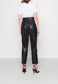 Pantalones de cuero negros de cintura alta con una textura suave y un corte ajustado. Combinados con una camiseta blanca y tacones negros con tiras.