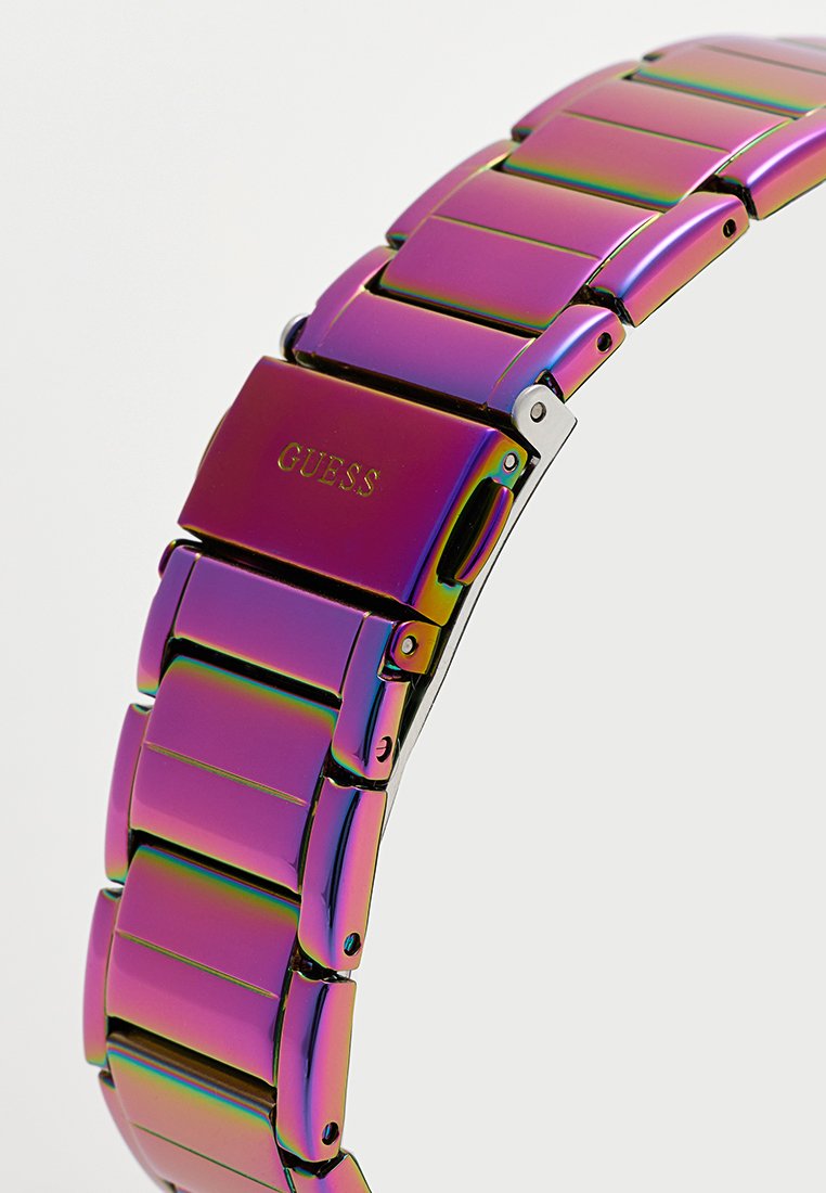 Bracelet de montre métallique avec une finition arc-en-ciel, présentant des maillons entrelacés, marqué "GUESS" en doré sur le fermoir.
