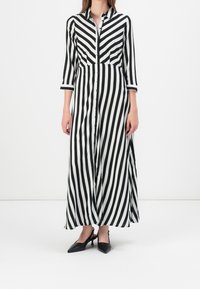 Robe longue à rayures noires et blanches avec un devant à boutons, un col, et des manches trois-quarts, associée à des talons aigus noirs.