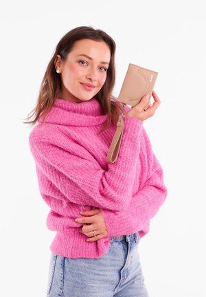 Beige cardholder with a wrist strap, featuring a textured surface and three circular accents, held against a white background by a person in a pink sweater.