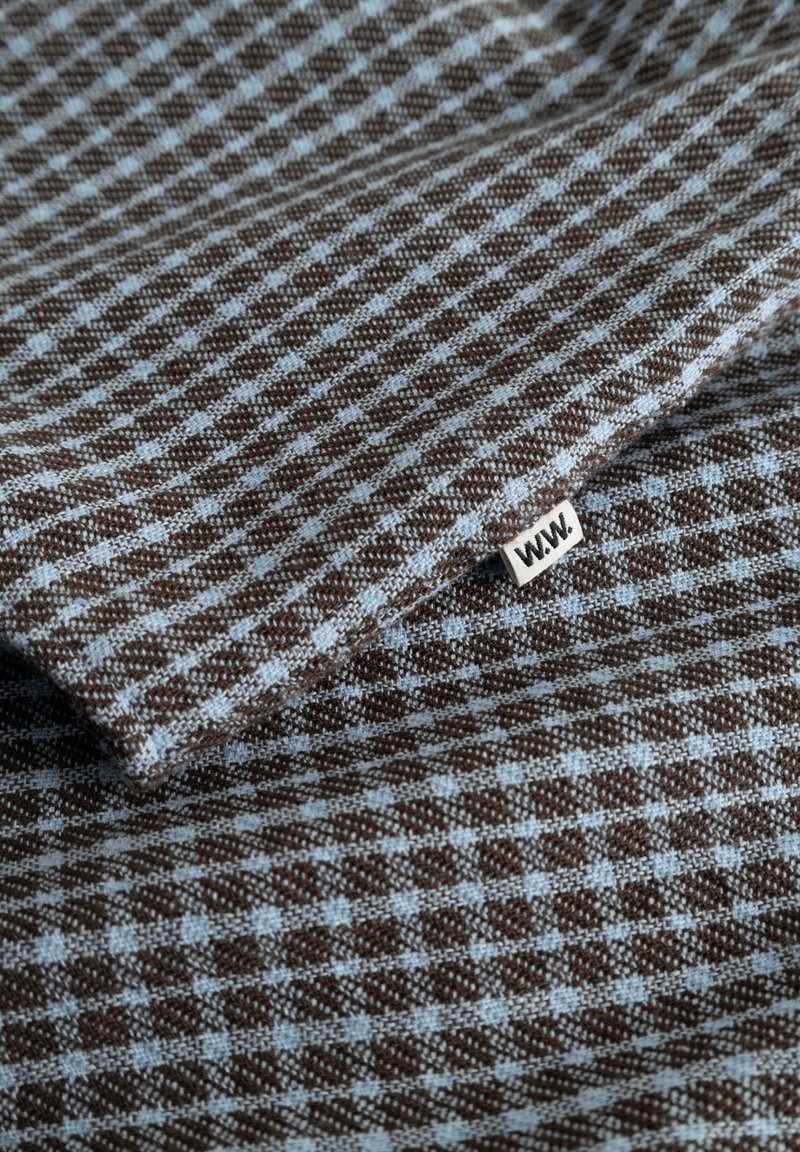 Brown and light blue checkered fabric with a small white tag labeled "WAW." folded on a flat surface.
