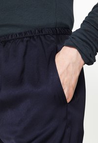 Navy blue trousers with a relaxed fit, elastic waistband, side pockets, and a smooth texture; paired with a dark green long-sleeve top.