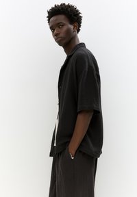 Maglietta nera a maniche corte con texture e colletto aperto, abbinata a pantaloni scuri e larghi, caratterizzati da cuciture distintive e design minimalista.