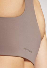 Brown sports bra with a smooth texture and a scoop neckline. Features embossed "GIRLFRIEND" branding on the side.