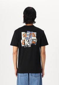 Schwarzes Baumwoll-T-Shirt mit einem bunten Grafikdesign auf der Rückseite, das überlappenden Text und abstrakte Formen in Blau-, Orange- und Grautönen zeigt.